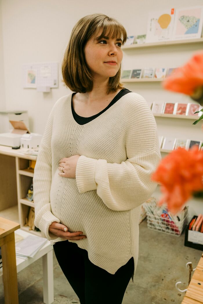 Pregnant woman in cozy sweater standing in a shop, reflecting on challenging Black Friday employee experiences.