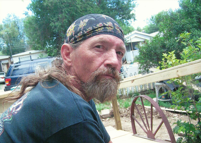 Middle-aged man with beard and bandana sitting outside near a wooden railing, related to missing woman&rsquo;s body discovery case.