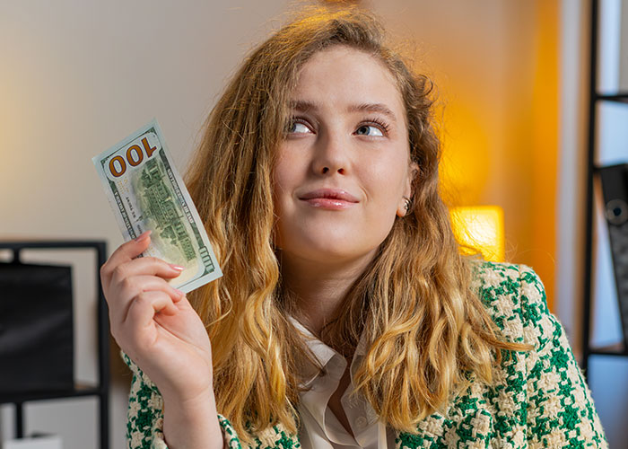Young woman holding a 100 dollar bill, pondering whether life is better in the USA or Europe debate.