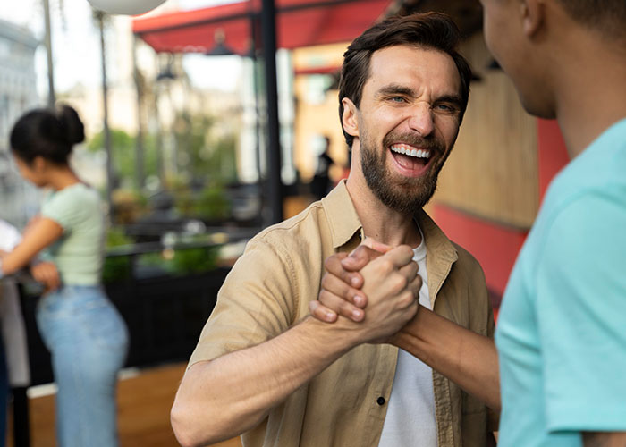 Two men smiling and shaking hands outdoors, symbolizing the debate on whether life is better in the USA or Europe.