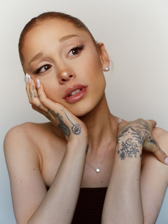Ariana Grande with tattoos on her hands, looking thoughtful and concerned in a close-up portrait.