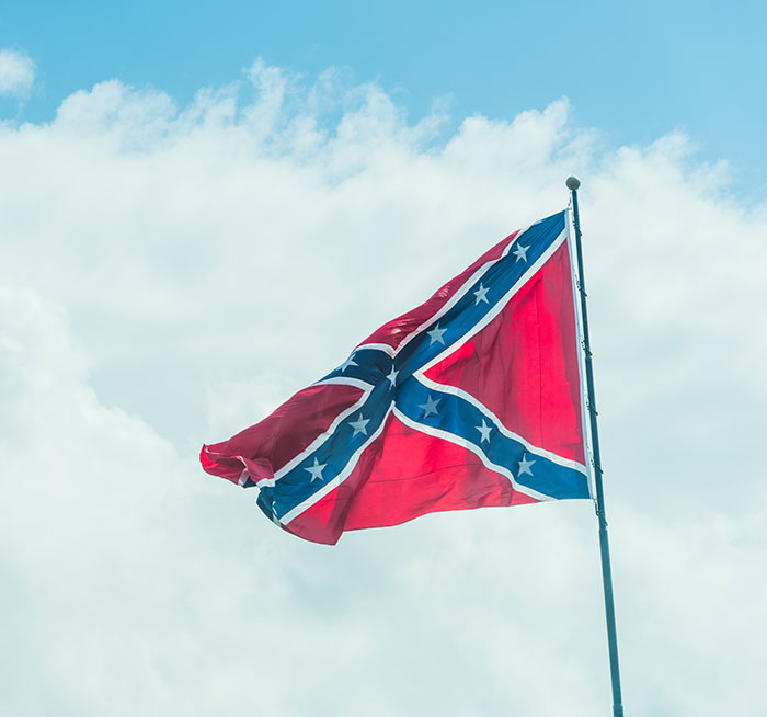 Confederate flag waving against the sky symbolizing controversy over racist name change and bullying at school.