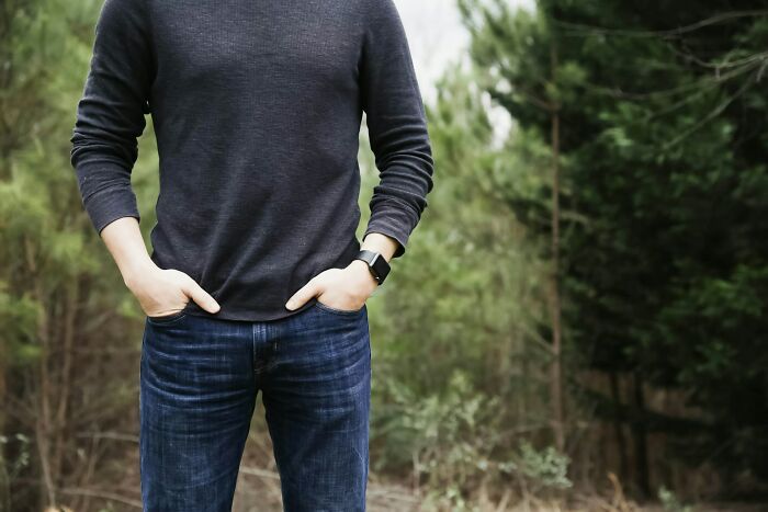 Person wearing a dark long-sleeve shirt and jeans standing with hands in pockets in a forest showing inherited traits from parents.