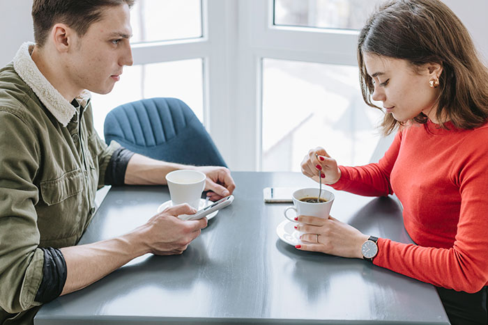 Bride and groom sitting apart at a table during a break, with the bride stirring coffee and the groom looking shocked. Bride and groom sitting apart at a table during a break, with the bride stirring coffee and the groom looking shocked.