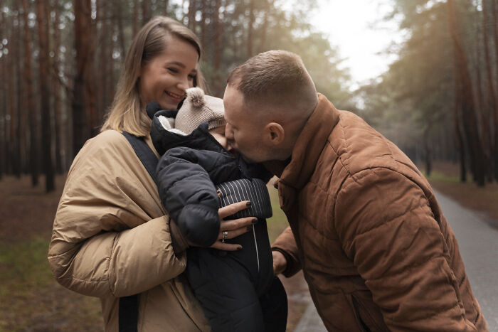 Happy adopted family outdoors in autumn forest, parents bonding with their baby during a walk on a path.