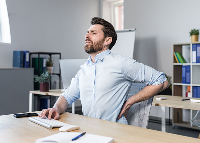 Man sitting in office chair rubbing his back, showing discomfort with his expensive $1.8K office chair at work. Man sitting in office chair rubbing his back, showing discomfort with his expensive $1.8K office chair at work.