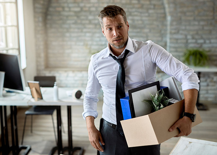 Man holding cardboard box with personal items, looking stressed after losing job over office chair dispute. Man holding cardboard box with personal items, looking stressed after losing job over office chair dispute.