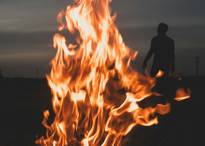 Large flames blazing in the dark with a silhouette of a person behind, representing weird and crazy ER stories.