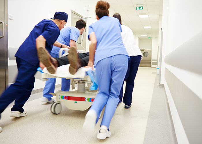 Medical staff rushing a patient on a stretcher through a hospital corridor in a chaotic ER scene.