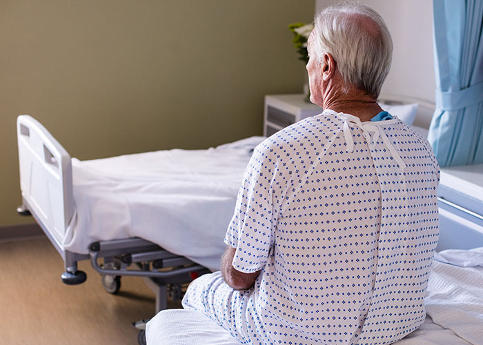 Elderly man in hospital gown sitting on bed in an ER room, highlighting unusual and crazy ER stories.