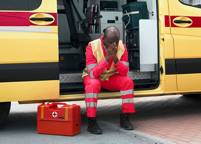 Stressed emergency responder sitting by ambulance with first aid kit, reflecting on weird and crazy ER stories.