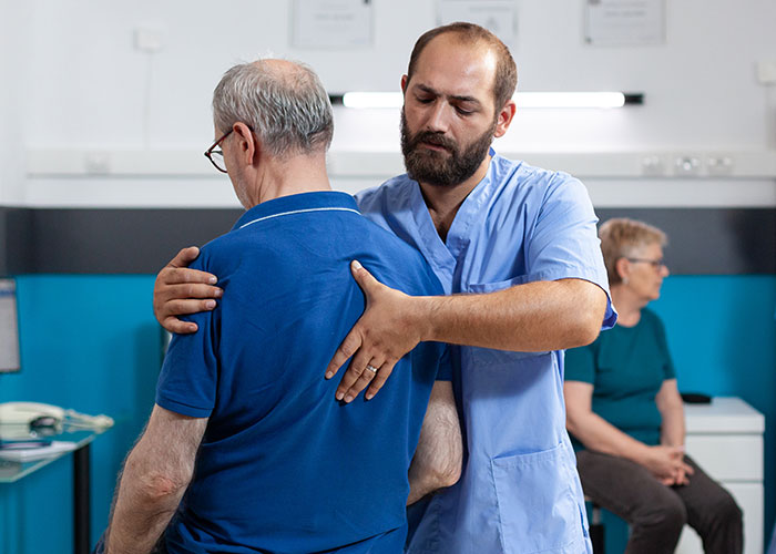 Male doctor examining elderly patient's back in a clinical setting, illustrating weird and crazy ER stories.