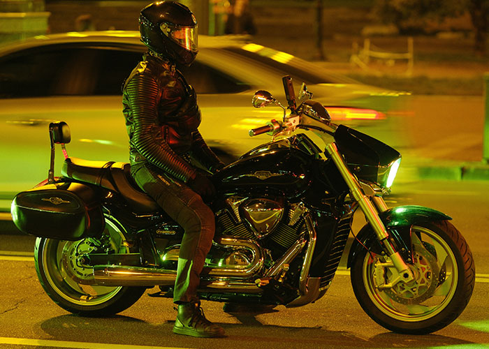 Motorcyclist wearing black leather jacket and helmet sitting on a cruiser bike at night, illustrating weirdest ER stories theme.