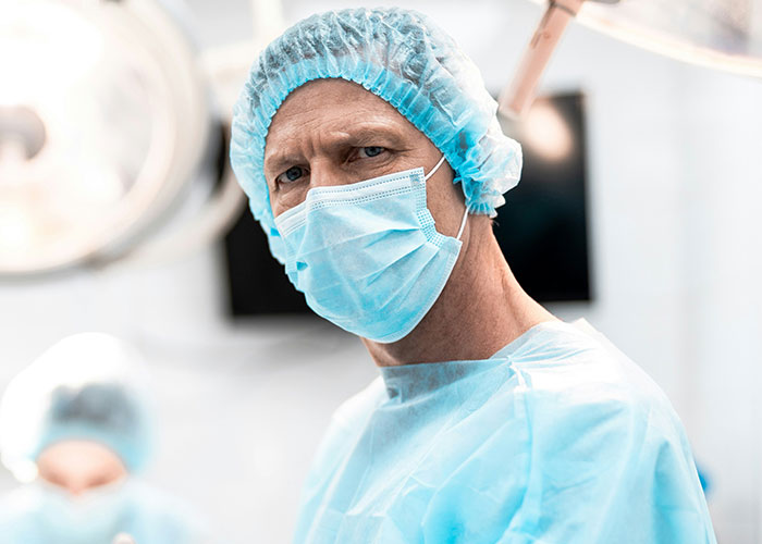 Male healthcare worker in protective gown and mask in an emergency room setting, highlighting weird and crazy ER stories.