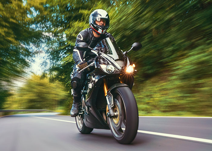 Motorcycle rider wearing full gear speeding on a forest road, illustrating weird and crazy ER stories.