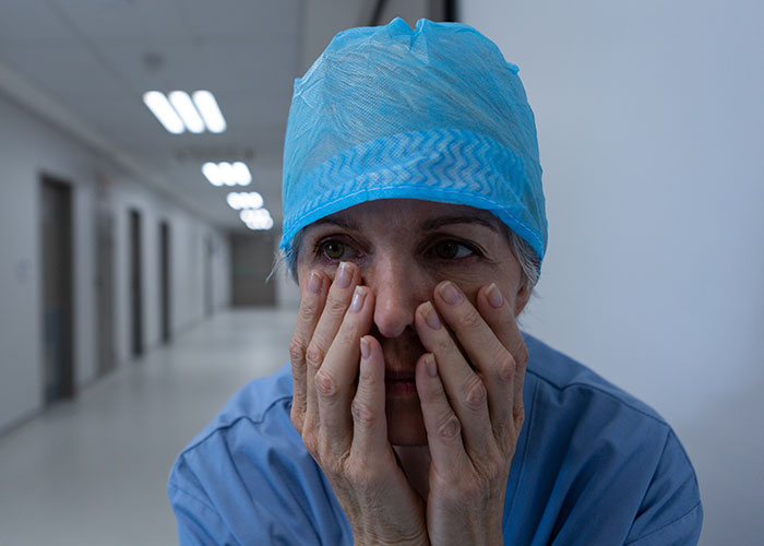 Stressed medical worker in scrubs and cap in empty hospital corridor reflecting intense ER stories.