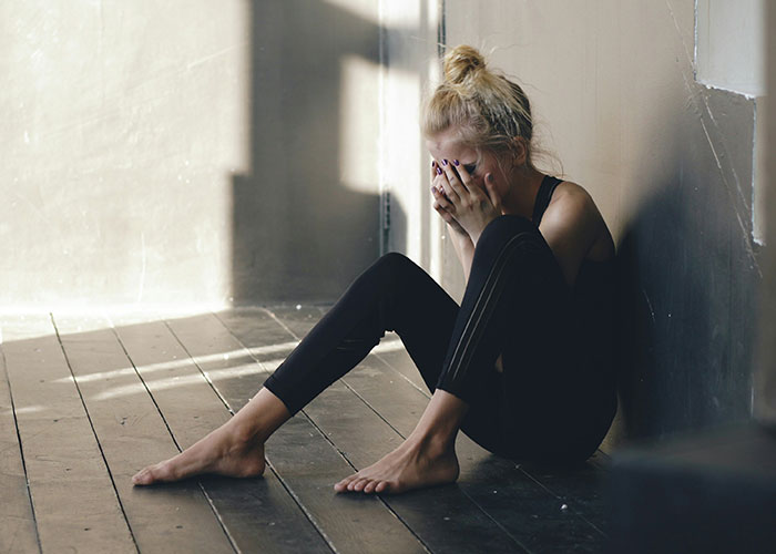 Young woman sitting on floor against wall, covering face with hands, depicting fear and narrowly avoided kidnapping experience.