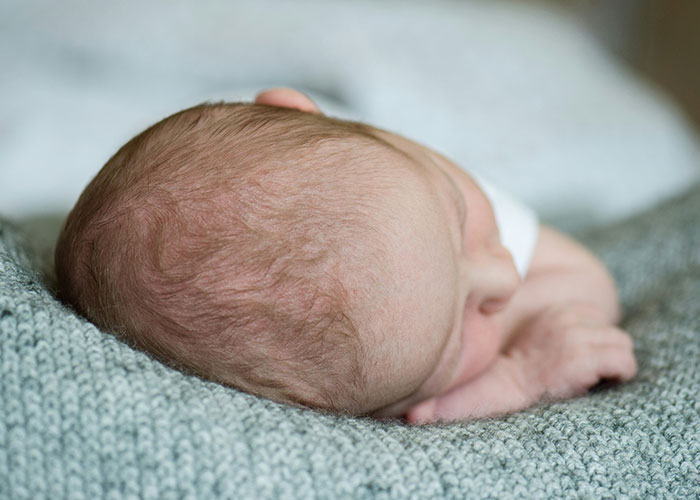 Newborn baby sleeping peacefully on a soft gray blanket, evoking themes of safety and narrowly avoided kidnapping fears.