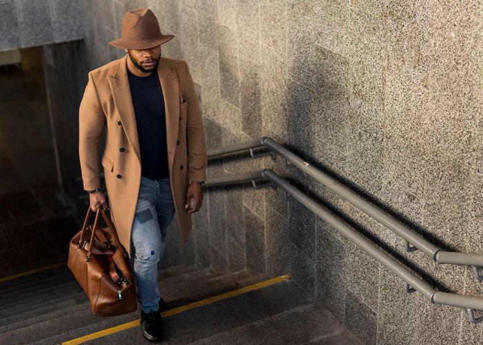 Man in a brown coat and hat carrying a leather bag walking up stairs, illustrating narrowly avoided being kidnapped concept.