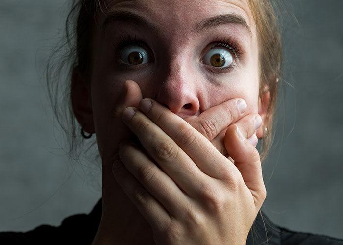 Young woman with wide eyes covering her mouth, illustrating fear and shock in disturbing online threads about kidnapping.