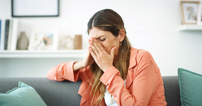 Woman feeling guilty after discovering boyfriend cheating, sitting on couch covering her face with hand at home.