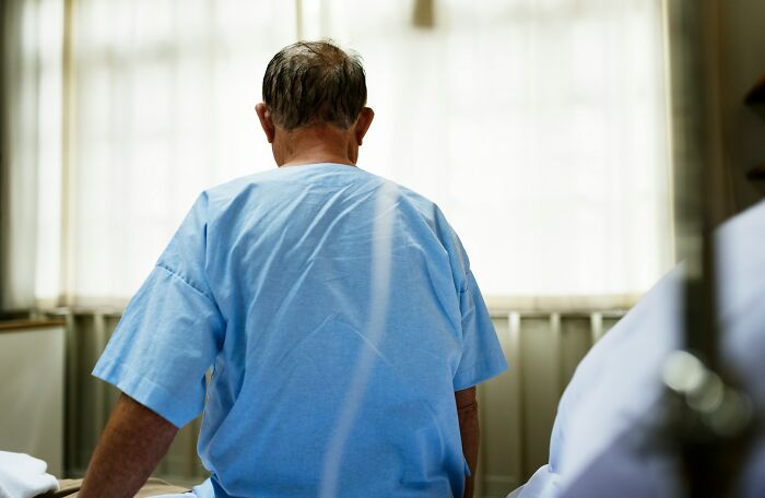 Elderly man in hospital gown sitting on bed, reflecting on heavy confessions people refused to take to their graves.