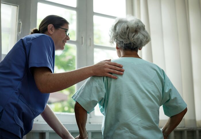 Doctor comforting an elderly patient by a window, illustrating eerie patient stories that still haunt doctors today.