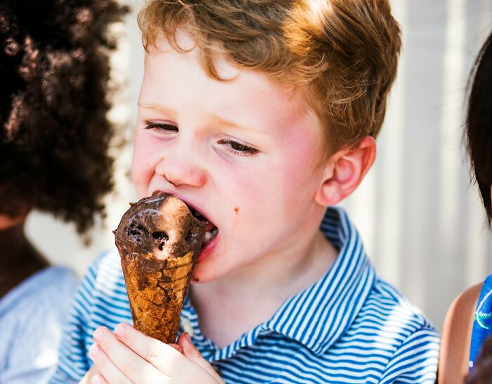 Young Nepo baby enjoying a chocolate ice cream cone on a sunny day with friends in a casual outdoor setting