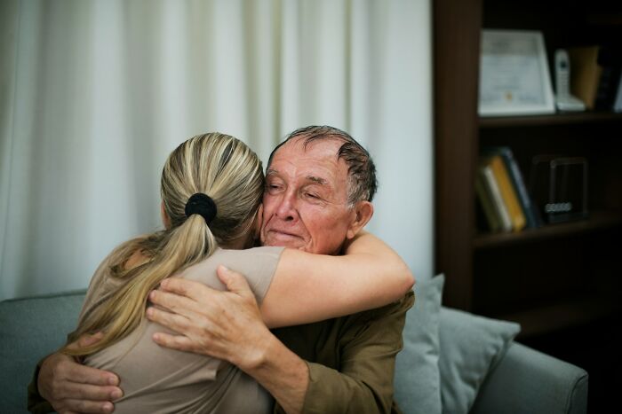 Elderly man and woman hugging closely, expressing comfort and emotional heavy confessions in a home setting.