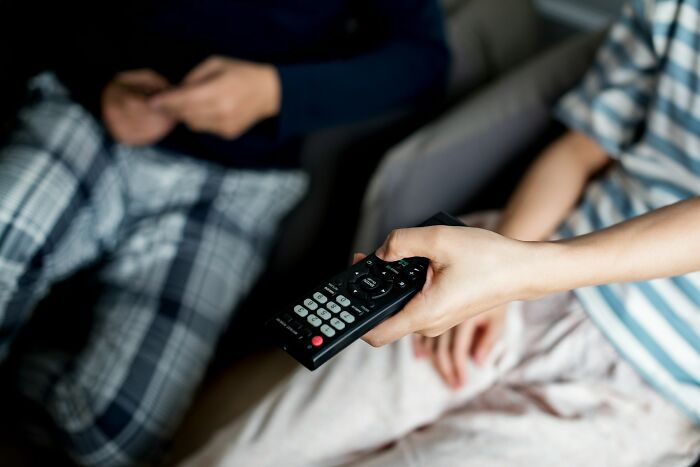 Two people sitting on a couch, one holding a remote control, illustrating surprising habits and secrets after moving in together.