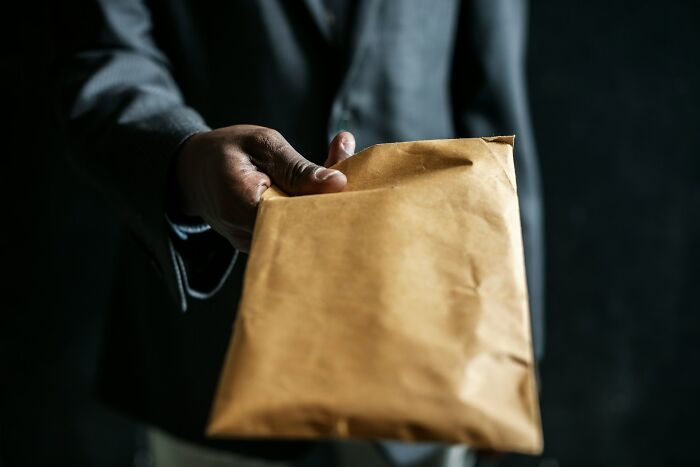 Person in a suit holding a brown envelope, representing one of the many times people fell for scams and their impact.