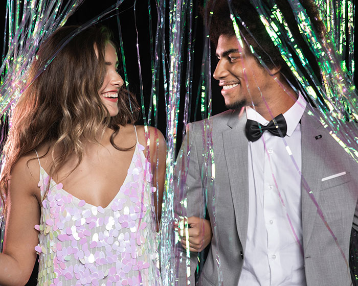 A smiling young couple dressed for a party, with shimmering decorations, representing driving a wedge between brother and his wife.