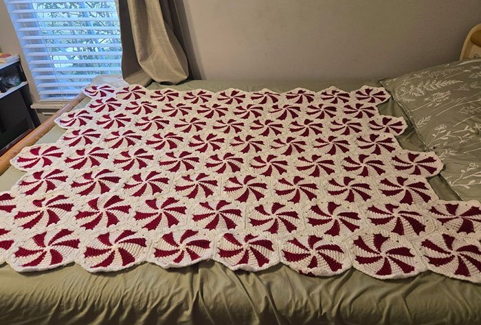 Crochet project featuring red and white pinwheel pattern blanket laid out on a bed by a proud crochet enthusiast.