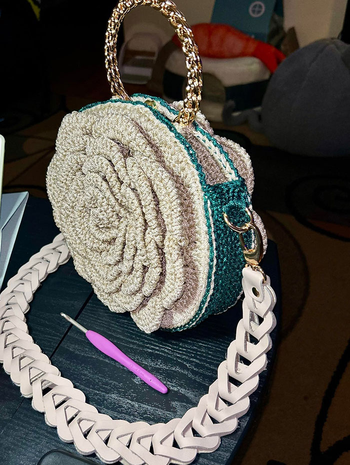 Crochet enthusiast’s detailed round handbag with braided strap and crochet hook displayed on black table.