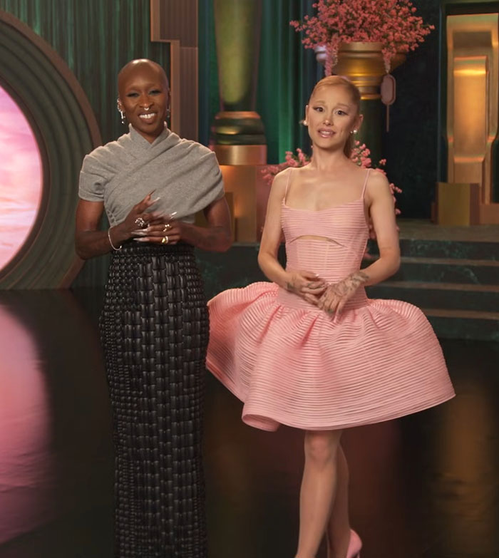 Two women stand in a colorful setting during a press event highlighting Ariana Grande revealing diagnosis amid Wicked tour.