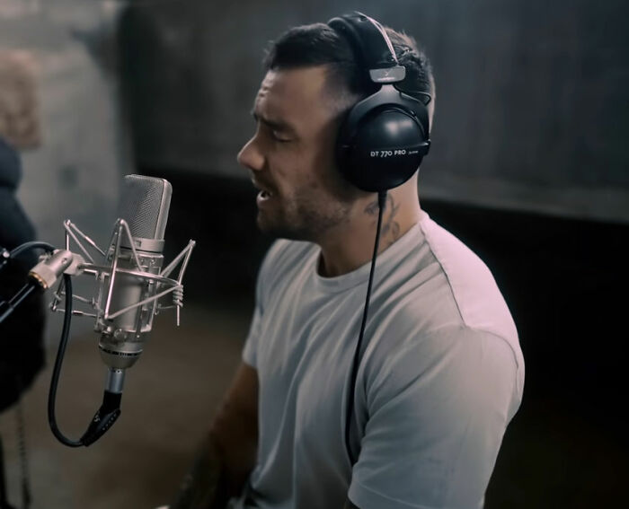 Man wearing headphones and white shirt speaking into a microphone, relating to Simon Cowell and Liam Payne mental health.