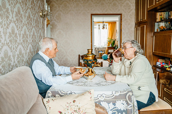 Elderly couple having tea at a table with a traditional samovar in a cozy vintage living room.