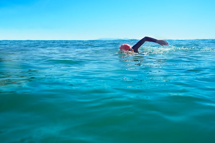 A swimmer in the ocean under clear blue sky, illustrating the powerful and dangerous nature of water.