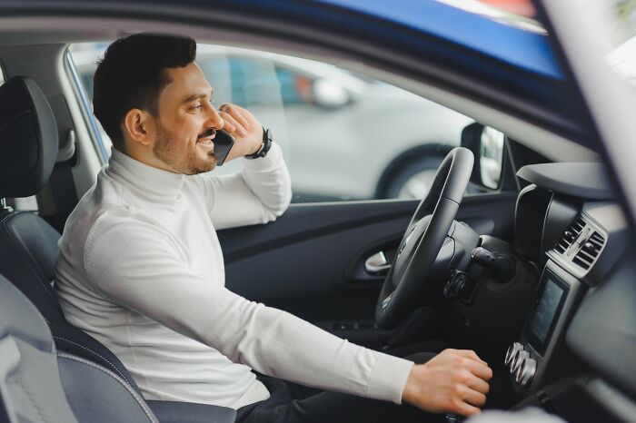 Man in a white turtleneck sitting in a car talking on a smartphone, illustrating water safety awareness concept.