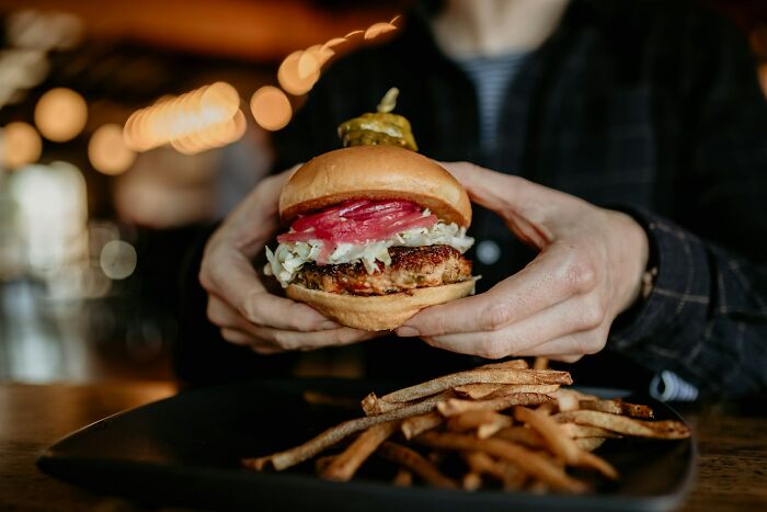 Person holding a burger with pickles and fries on a plate, illustrating internet users sharing what isn’t a scam.