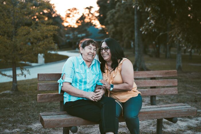 Two women sitting on a park bench, sharing a joyful moment, representing family and golden child stories.