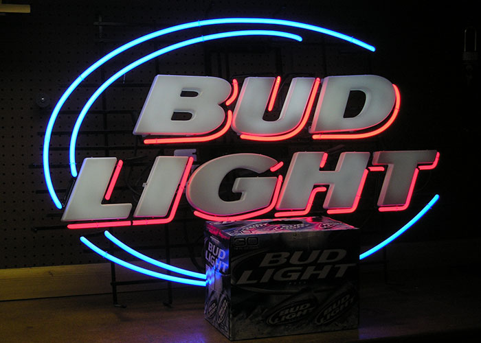 Bud Light neon sign with a box of Bud Light cans, illustrating companies competing for corporate Darwin award.