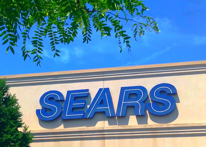 Sears store sign on building exterior under clear sky, representing companies competing for corporate Darwin award.