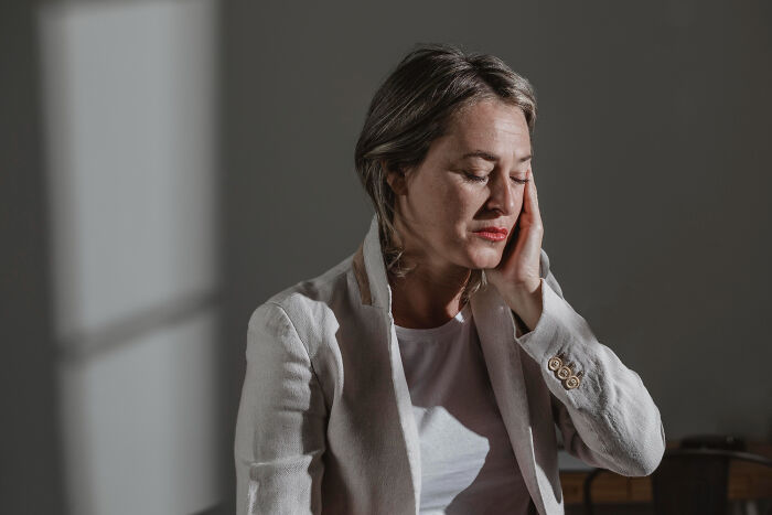 Middle-aged woman with closed eyes and hand on face, reflecting on dating older people stories and being single.