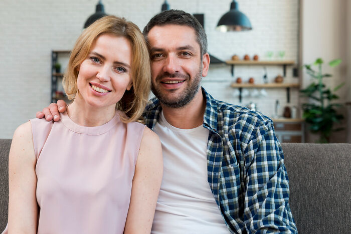 Smiling couple sitting close on a sofa at home, illustrating dating older people stories from a single perspective.