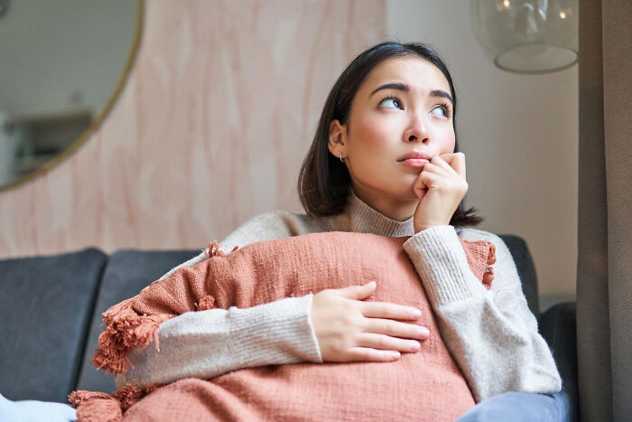 Young woman sitting on a couch hugging a pillow, reflecting on dating older people stories while single and thoughtful.