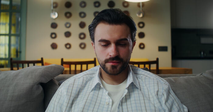 Man sitting alone on a couch, looking thoughtful and reflective, related to dating older people stories single.