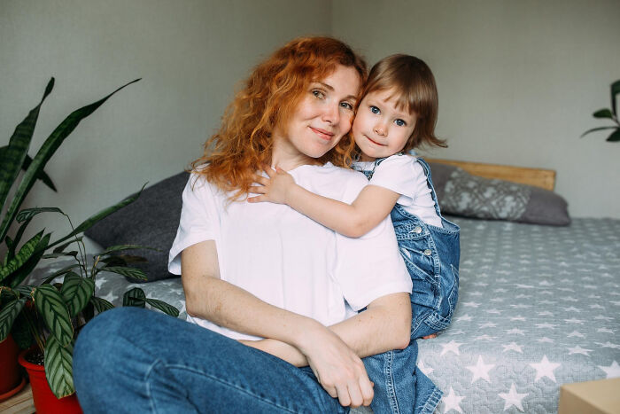 A woman with red hair sitting on a bed with a young child hugging her, depicting dating older people stories single.