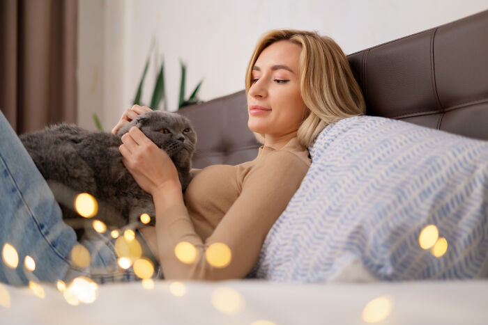 Young woman relaxing on a bed with a gray cat, representing comfort in dating older people stories single.