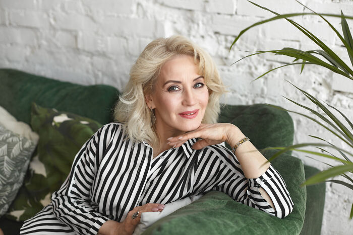 Mature woman smiling and relaxing on a green couch, representing dating older people stories and single lifestyle.